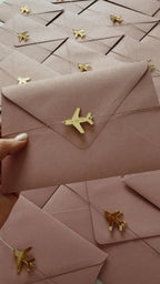 Pink envelopes with gold airplane charms for wedding invitations