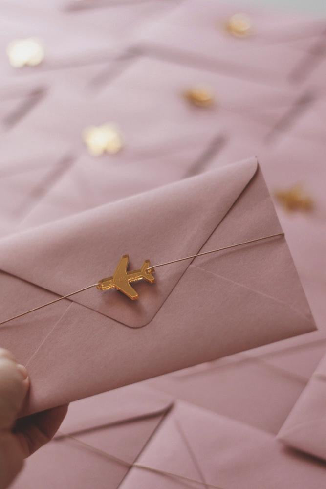 Gold airplane wedding charms on pink envelope